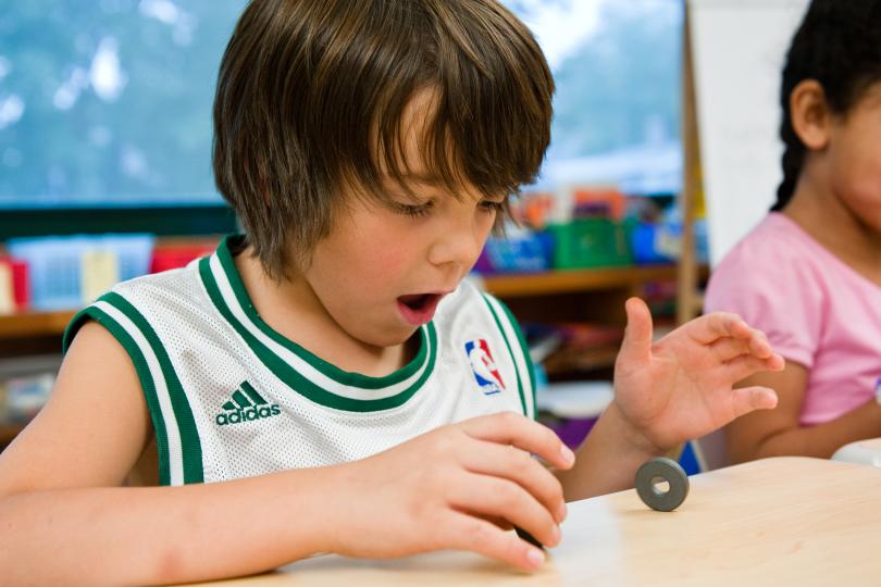 a boy in a classroom has a "wow" expression on his face as he plays with magnets
