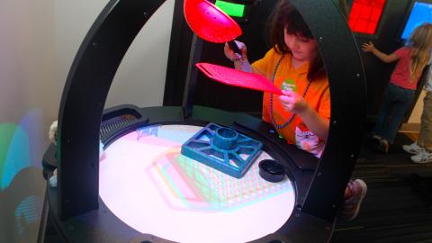 A girls holds plastic objects over a light table to create shadows