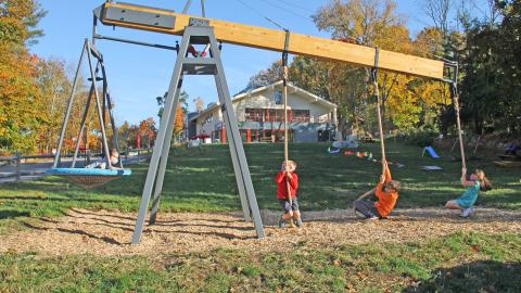 photo of a giant lever with a basket swing on one end, 3 pulley ropes on the other end, with kids in the basket and hanging on the ropes