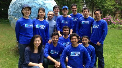 large group of people in matching shirts pose before a large globe