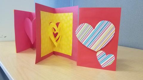 Three handmade cards made of construction paper and decorated with hearts are standing open on a table