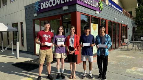 five people stand in front of a museum entrance, four are holding white envelopes