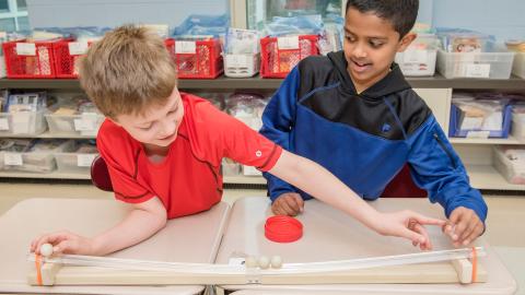 two boys do a force and motion experiment with balls and ramps
