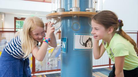 two girls listen into glass tubes and laugh together