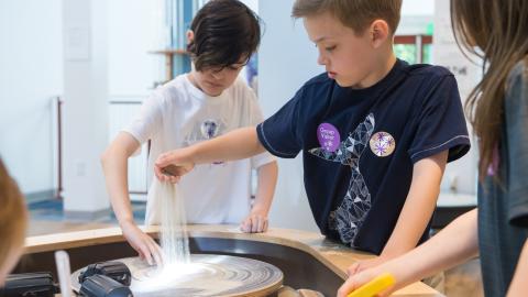 two boys pour sand onto a spinning disk