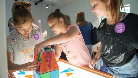 three girls work together to build a structure from MagnaBlocks on a lighted table