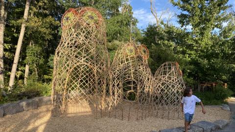 a young girl stands near a 10' bamboo sculpture of a family of 3 owls