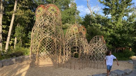 a young girl stands near a 10' bamboo sculpture of a family of 3 owls