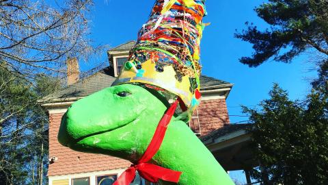 the head of a dinosaur statue, wearing a large cone-shaped party had