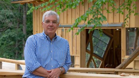 a man leans on a railing outside of a treehouse