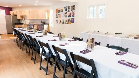 a long table is set with a white tablecloth and purple napkins