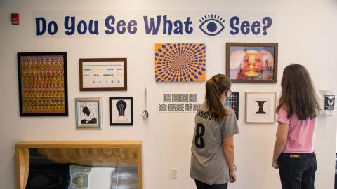 two teen girls look at an optical illusions exhibit together