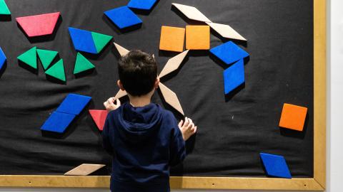 a boy stands and plays at a board of moveable geometric shapes