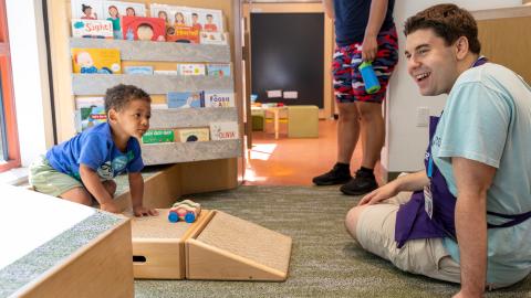 a young boy and a staff member play with cars on a ramp