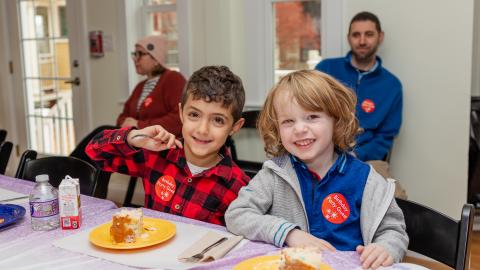two young boys sit at a table with plates of birthday cake