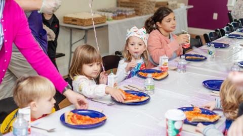 young children sit at a table and have pizza during a birthday party