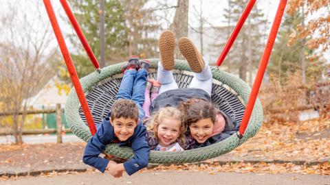 3 children swing in a large saucer-shaped swing