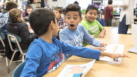 two boys look at each other in surprise and awe as they work on a science experiment together