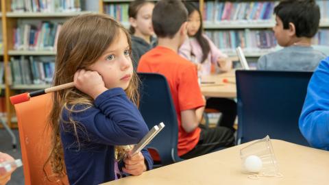 a young girl holds a tuning fork up to her ear
