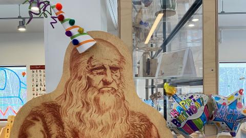 a life-sized cutout form of Leonardo da Vinci, wearing a party hat
