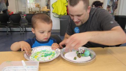 A man and boy each have paper and paint in aluminum pie plates and are rolling balls in the paint