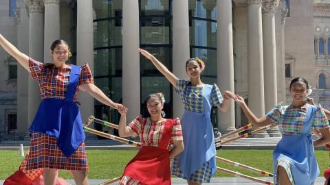 Four female dancers in traditional Filipino costumes pose with arms out