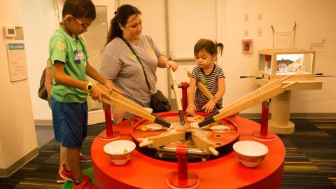 a mom and two kids use an exhibit of giant chopsticks