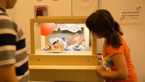 a young girl look into a light-up exhibit of a puppet show