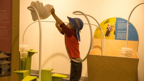 a small boy reaches up over his head to move plastic pieces along a curved rod
