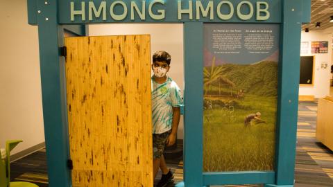 a boy walks through the door of a model of a Hmong home