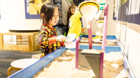 a young girl explores a sand exhibit