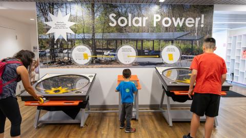 3 people play at an exhibit about solar cell technology