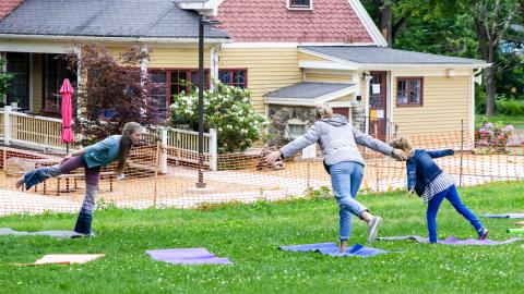 a yoga instructor and two yoga students do a yoga pose outside on a lawn