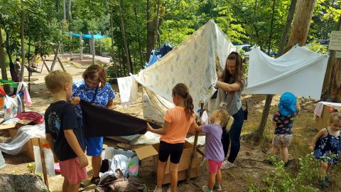 A group of kids and adults hanging blankets between trees to build forts