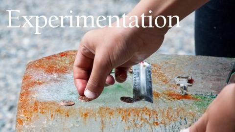 a photo of a boy's hand as he experiments with placing coins, salt and food coloring on a giant block of ice