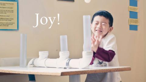 a young boy is surprised and delighted as a ping pong ball pops out of a tube and he tries to catch it