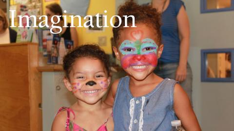 two young sisters with painted faces smile big for the camera