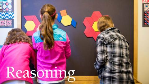 three children work side-by-side arranging geometric shapes on a magnetic wall