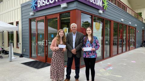 two teenagers and a man stand in front of a building, the teens are holding envelopes