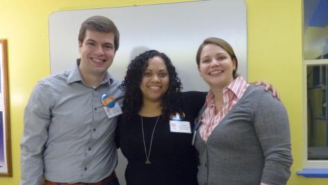 Three adults wearing nametags stand together, smiling