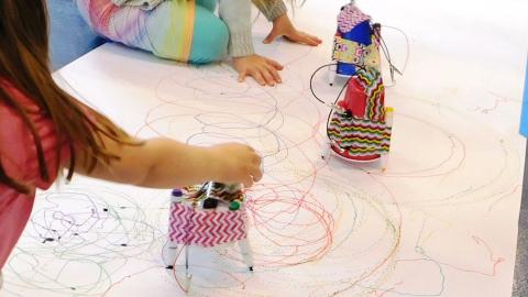 Children guide small robots as they make marks on paper