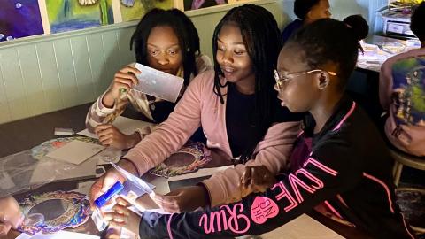 three students explore light and color in a darkened classroom
