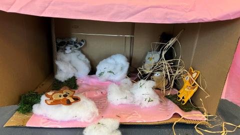 The inside of a box covered in a pink blanket. Inside are small piles of cotton with figures of different animals sitting on them.