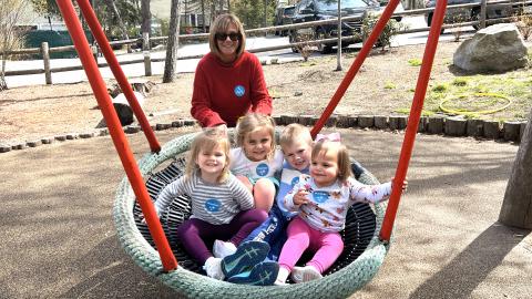 a grandmother pushes four young children in a large swing, outdoors