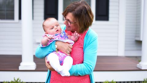 a grandmother holds her grandbaby, smiling and singing to her