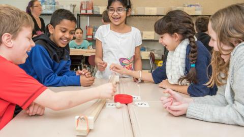 Middle school children with a ramp and a ball on a desk for science workshop