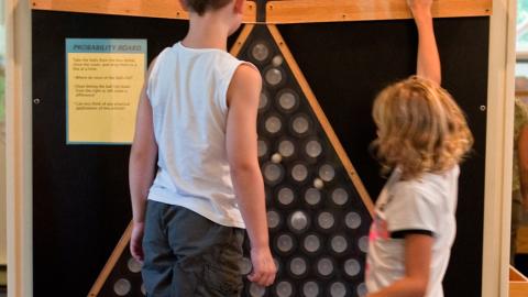 two children drop small balls into a wall-mounted frame that will sort them into columns