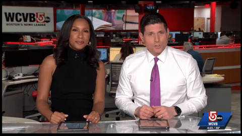 two television news anchors sit at the news desk