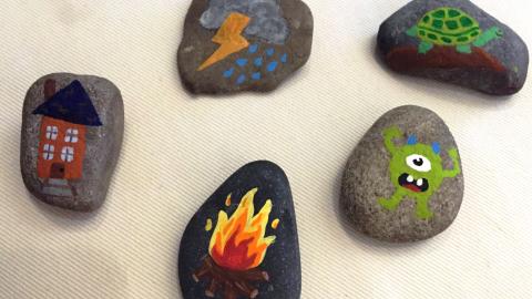 Five rocks on a table. Each has a different picture painted on: House, lightening, fire, turtle, and monster