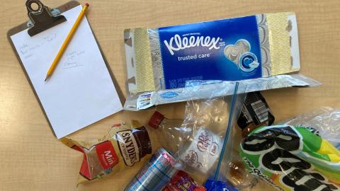 a clipboard with pencil on a table next to trash - kleenex box, food wrappers, cans, etc